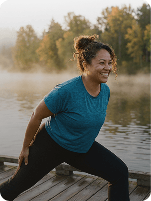A woman stretching on a lakeside dock at sunrise